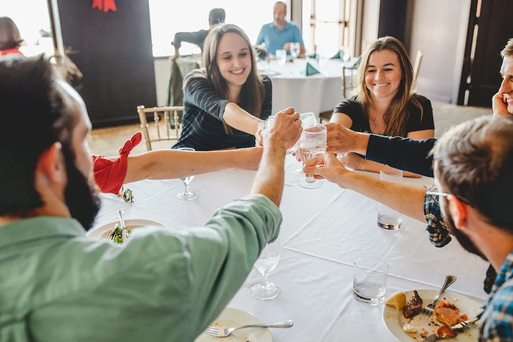Smiling people clink clear glasses during a restaurant toast.