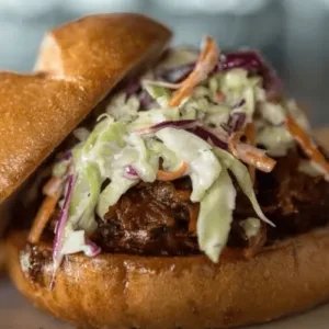 Close-up of a pulled pork sandwich with coleslaw on a toasted bun.