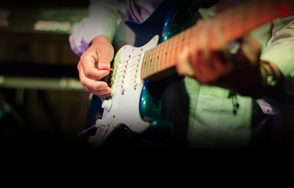 Hands strumming a blue and white electric guitar under colored stage lights.