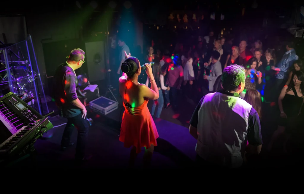 Band on stage illuminated by colorful spotlights, with a blurred dancing crowd.