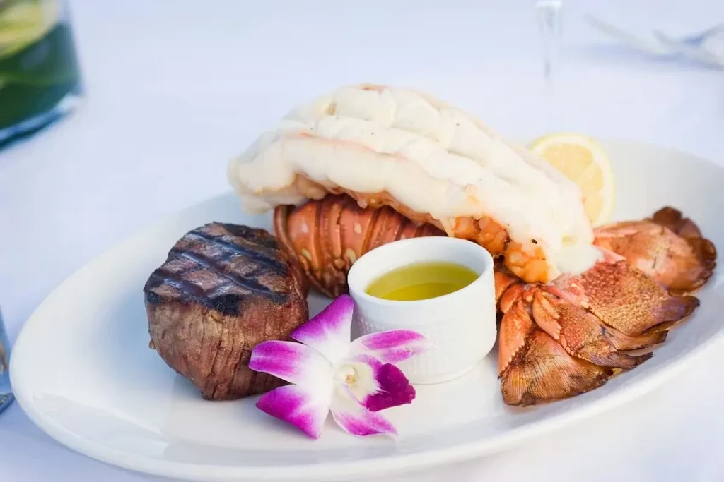 Grilled surf and turf with steak, lobster, butter, lemon, orchid.