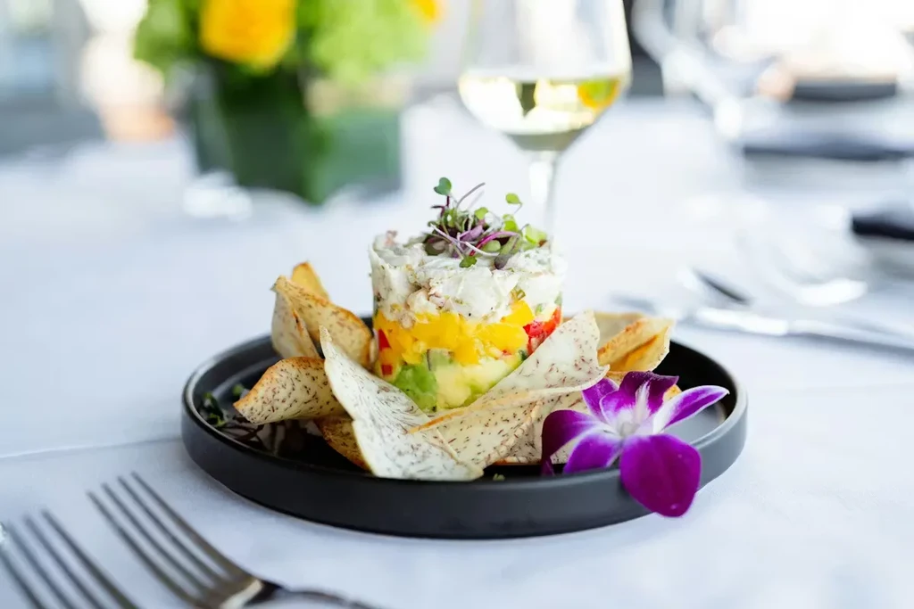 Layered seafood, mango, avocado stack with chips, microgreens, and orchid.