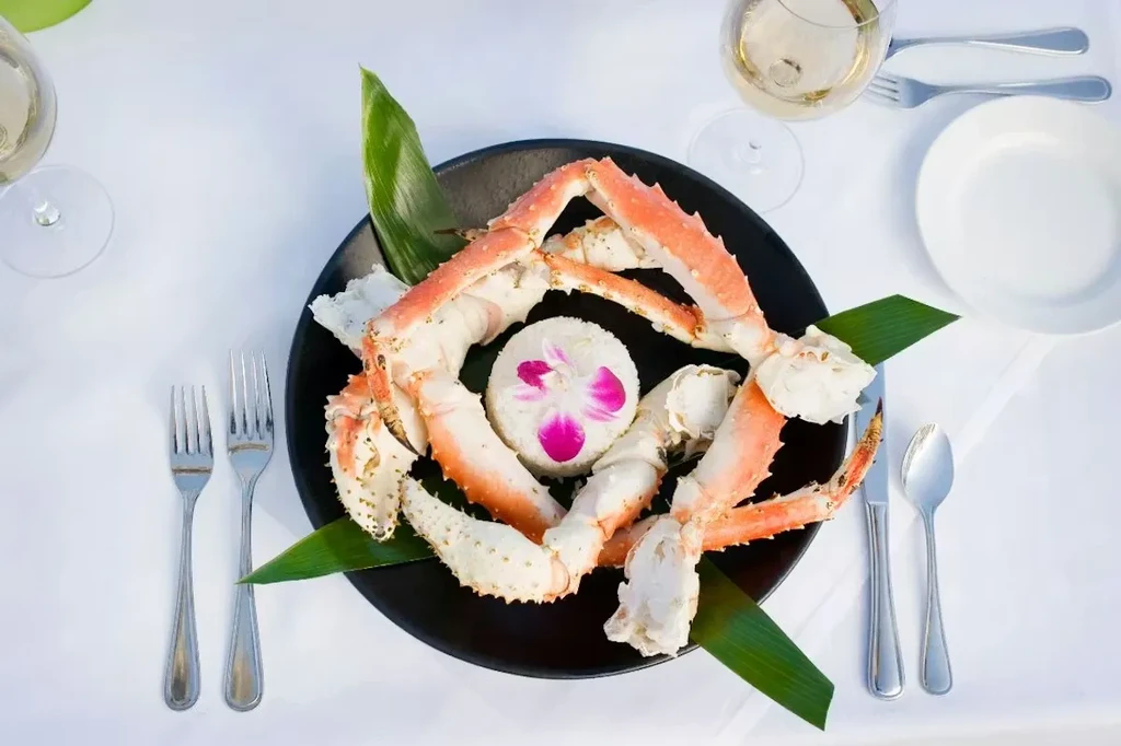 Overhead: Crab legs, rice, fuchsia orchid, and cutlery on a dark plate.