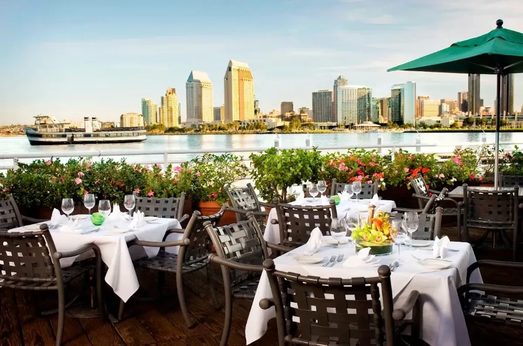 Set outdoor patio with plants overlooks water and city skyline.