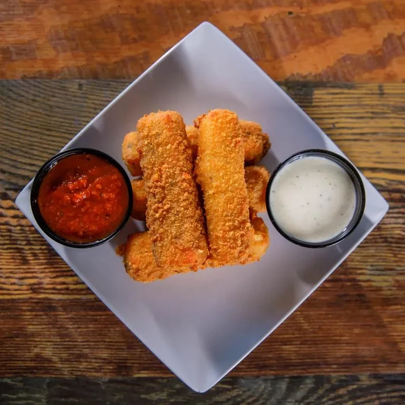 Overhead plate of fried appetizers with red and creamy sauces on wood.
