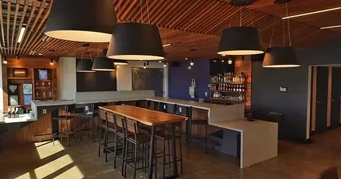 Modern bar interior with light counter, dark table, and wooden ceiling.