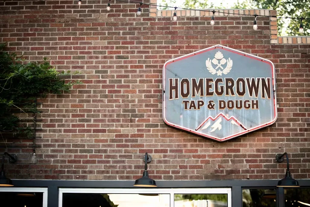 Rustic brick wall with Homegrown Tap & Dough sign and string lights.