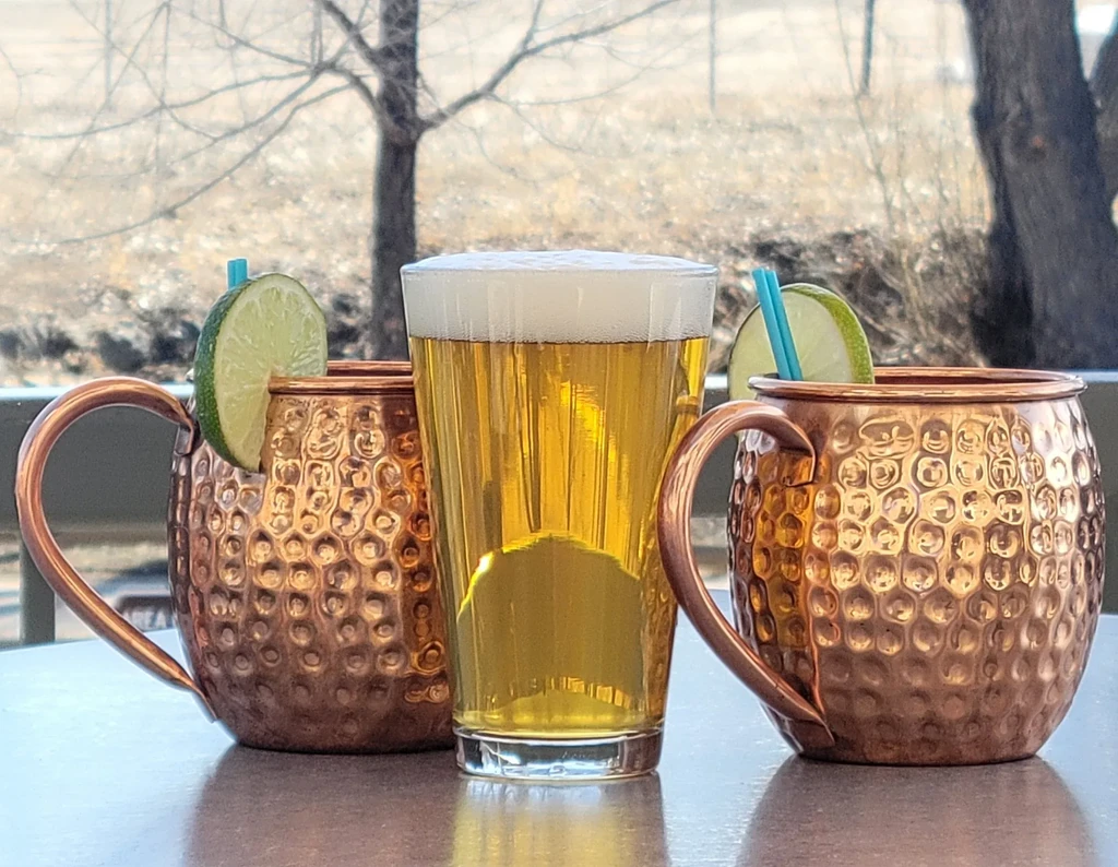 Beer and two copper Moscow Mules with lime on an outdoor table.