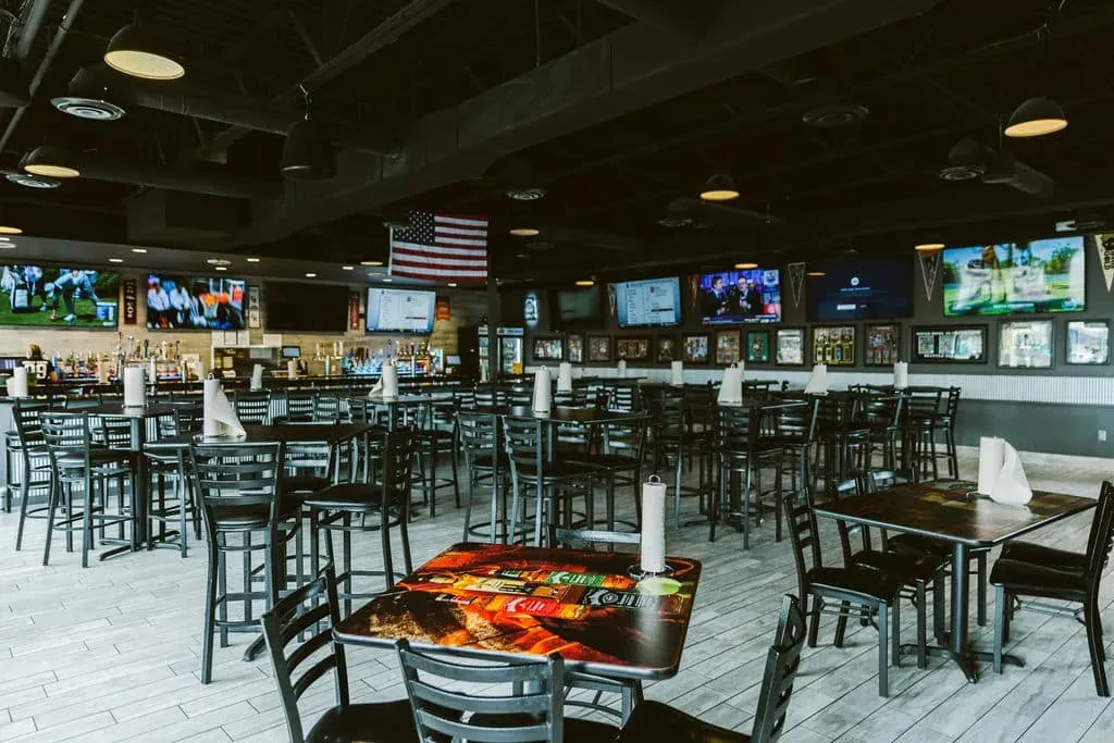 Modern sports bar interior with high-top seating, TVs, and American flag.