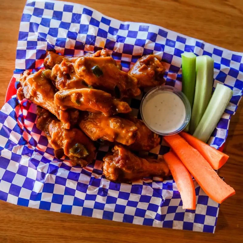 Buffalo chicken wings, ranch dip, celery, and carrots on a table.