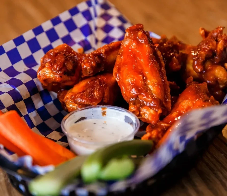 Buffalo chicken wings, creamy dip, and vegetable sticks in a basket.