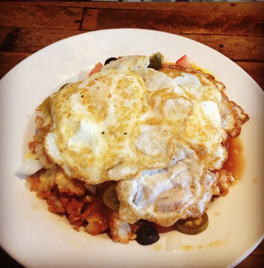 Overhead red-sauced dish with two fried eggs, cheese, olives, jalapeños.