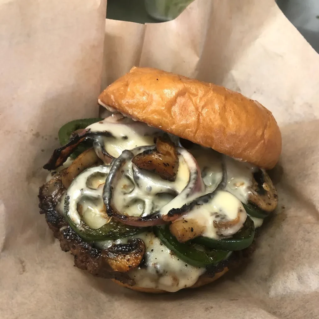 Gourmet burger with char-grilled patty, melted cheese, peppers, onions, mushrooms.