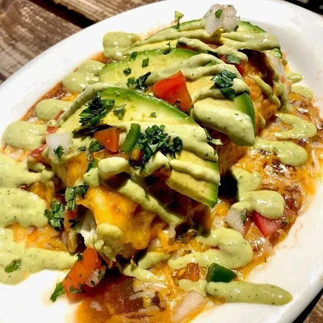 Vibrant dish with avocado slices, melted cheese, tomatoes, and green crema.