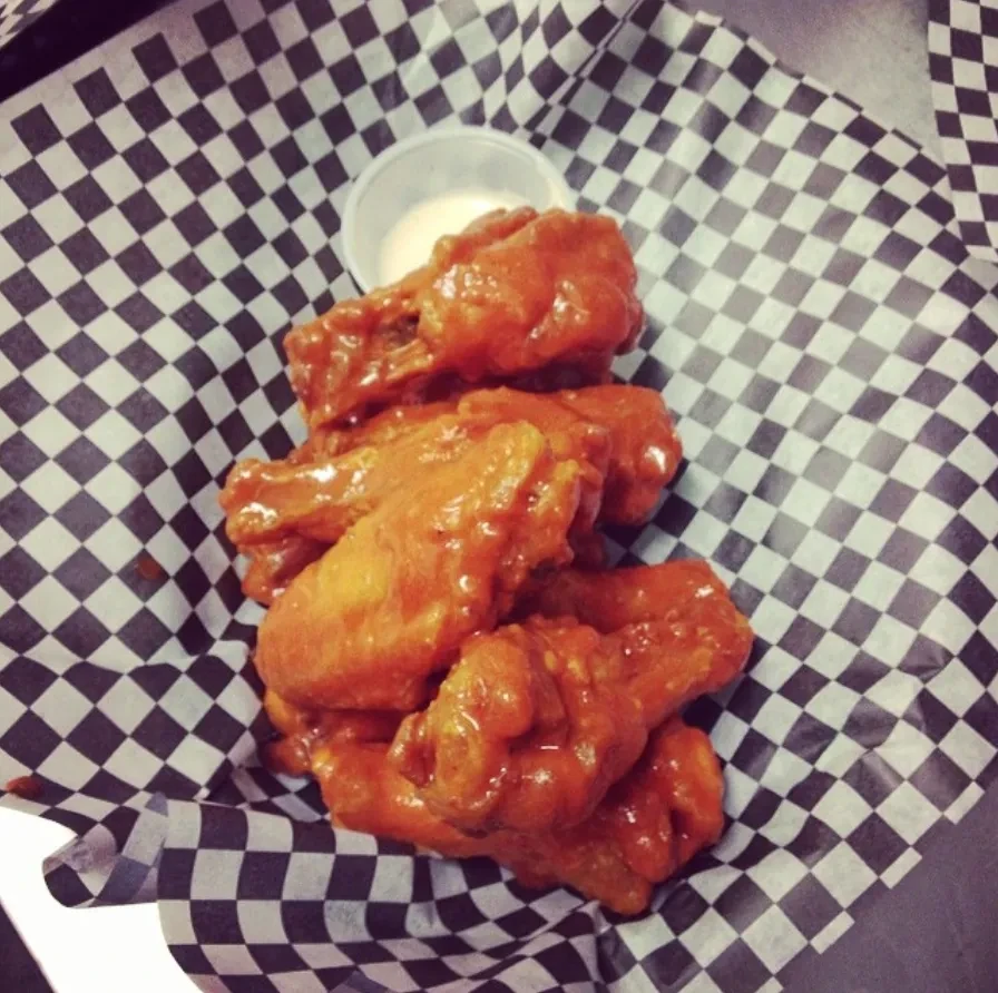 Close-up of buffalo wings in a checkered basket with dipping sauce.