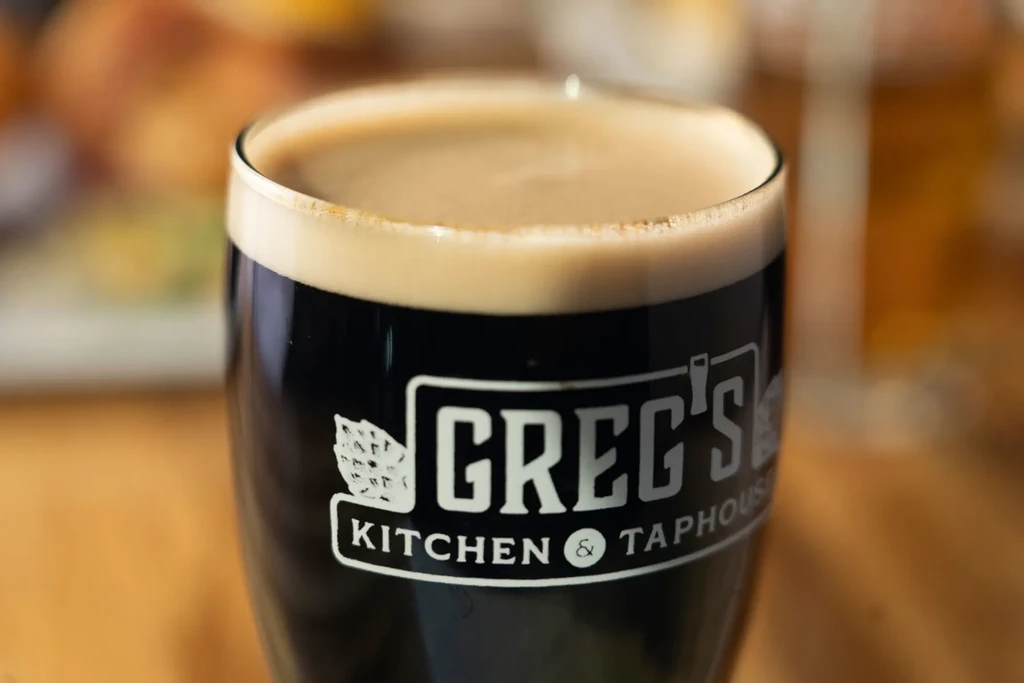 Greg's Kitchen glass filled with dark stout beer, creamy head.