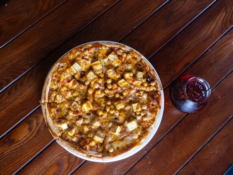 Sliced pizza with paneer and chickpeas, a cold fruit drink.