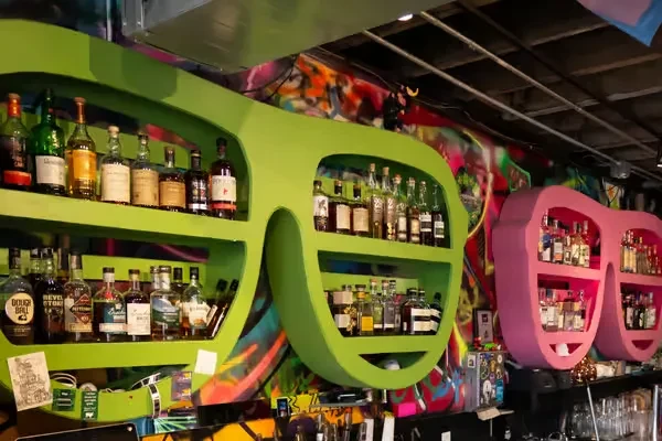 Vibrant bar with eyeglass shelves displaying liquor bottles and graffiti art.