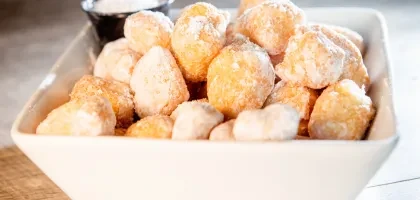 White bowl filled with golden-brown powdered sugar donut holes.