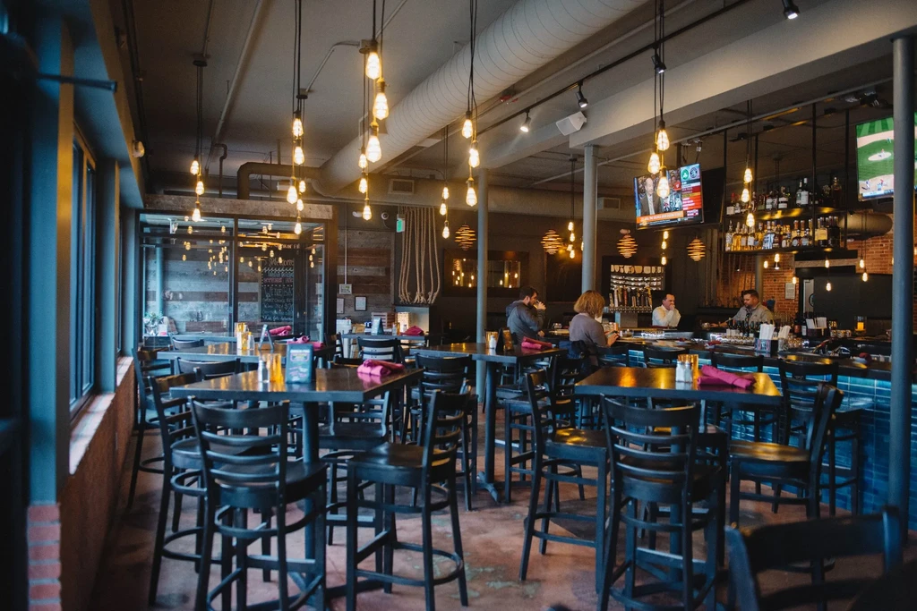 Modern bar interior with industrial design, warm lighting, and patrons.