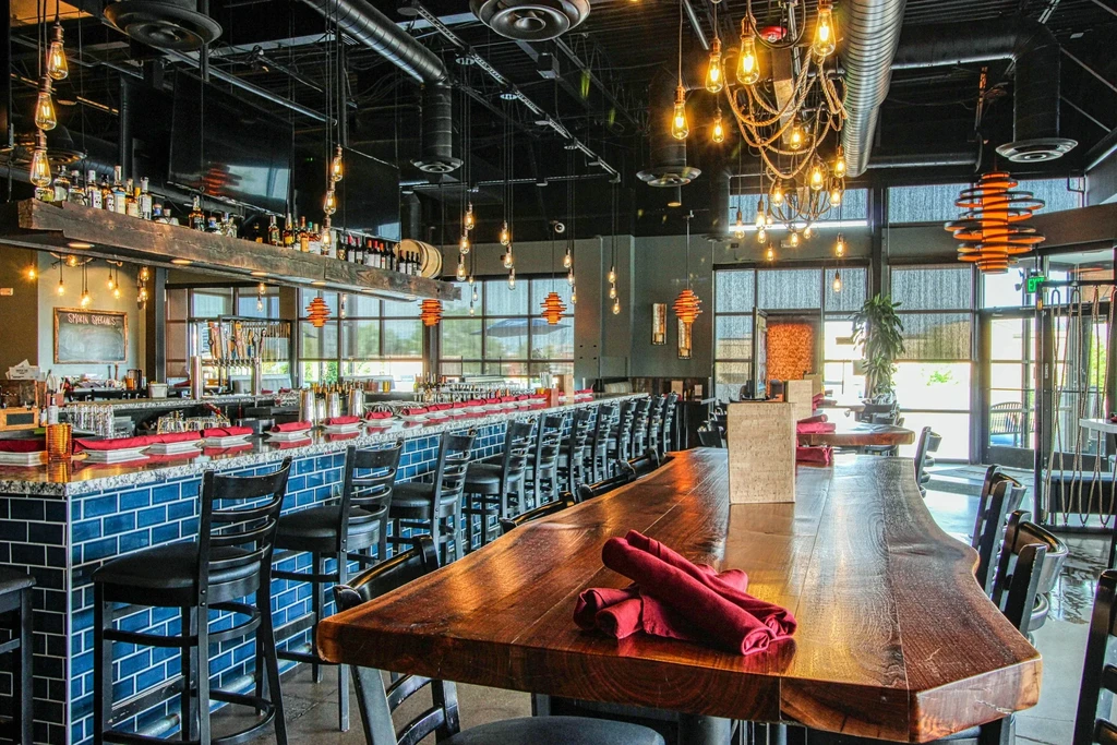 Modern-industrial restaurant with blue-tiled bar, communal table, and Edison lighting.