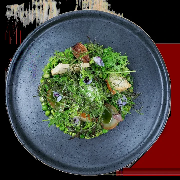 Artistic green pea appetizer with leaves, croutons, and edible flowers.