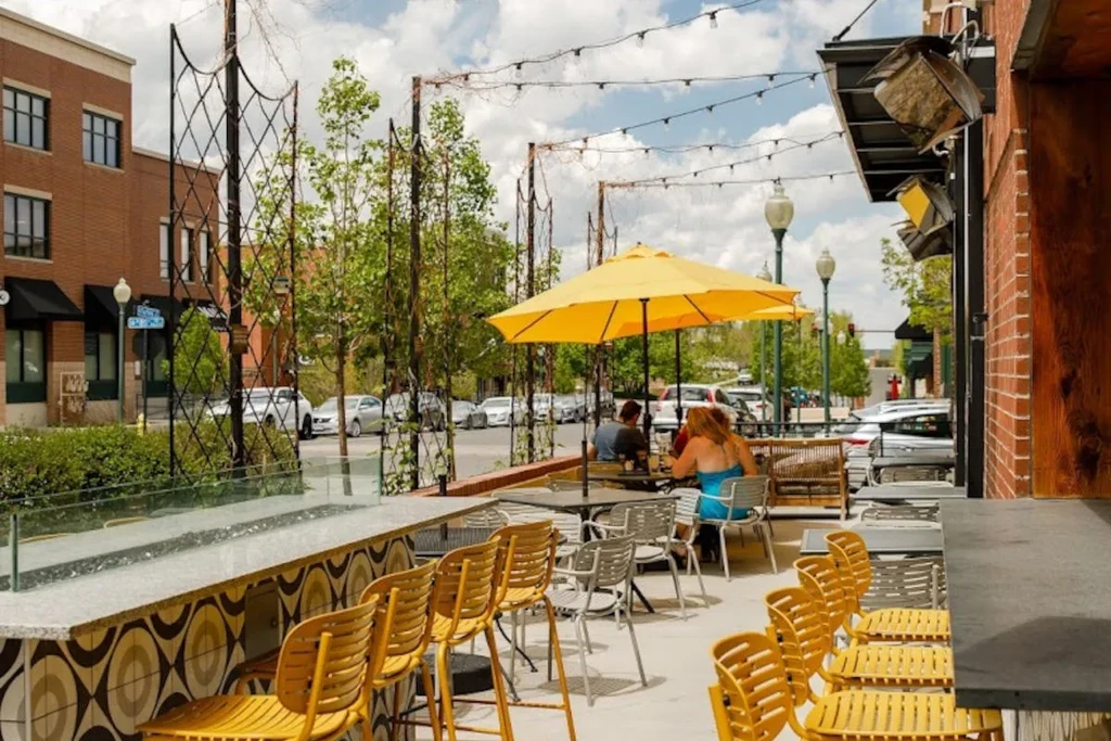 Bright outdoor restaurant patio with yellow bar, umbrella, and diners.