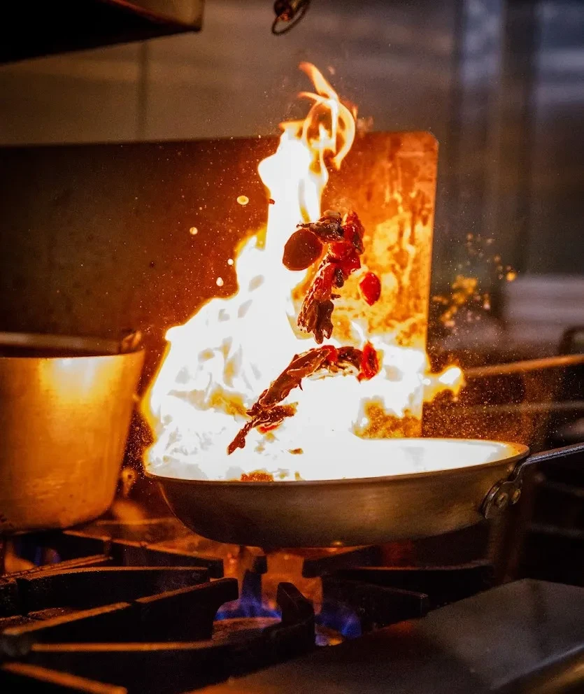 Food igniting in bright white and orange flames from a cooking pan.