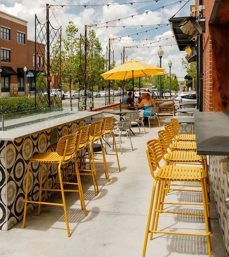 Outdoor restaurant patio with yellow bar stools and umbrella on a sunny day.