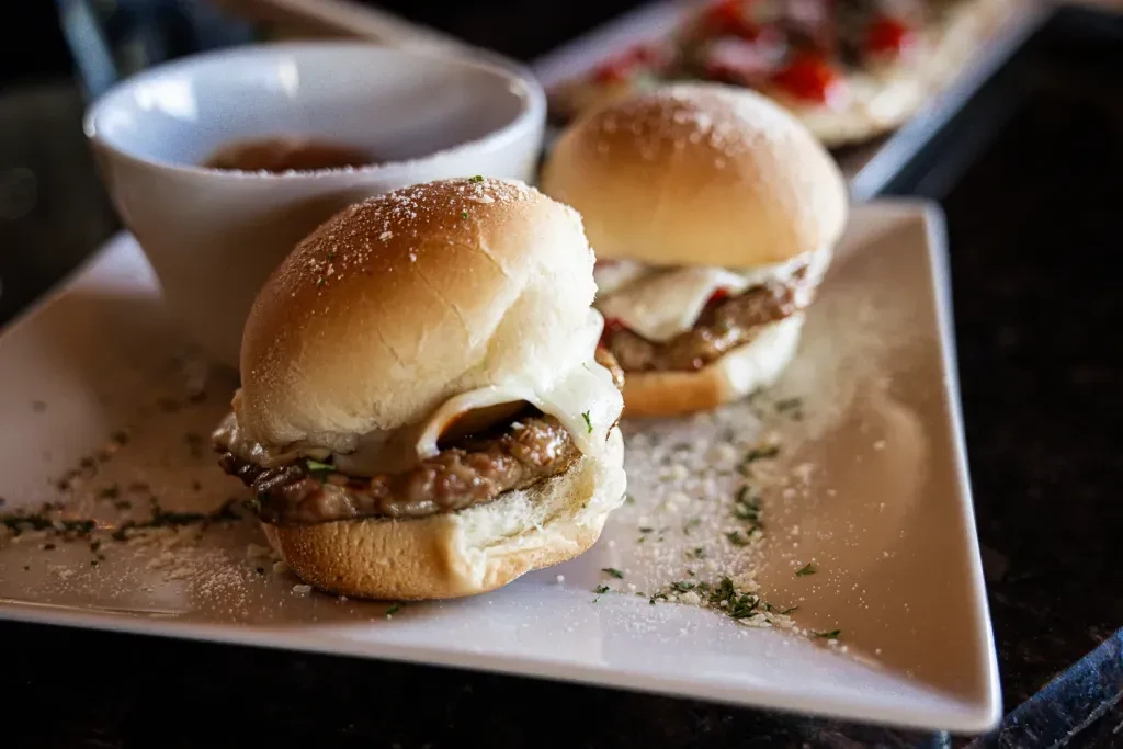Two sliders with melted cheese, herbs, and dipping sauce.