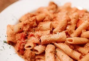 Close-up of tube pasta with creamy tomato sauce, cheese, and herbs.