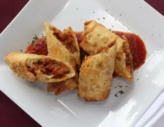 Golden-brown fried rolls, one cut open, on red sauce with herbs.