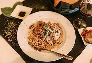 Overhead view of creamy pasta, red wine, and appetizers.