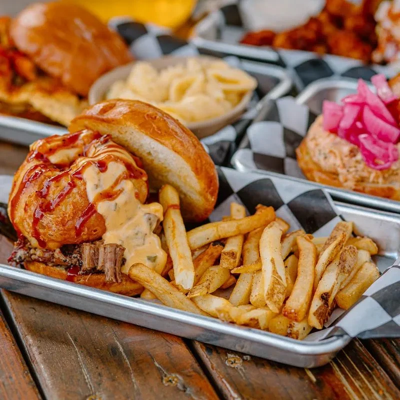 Shredded meat sandwich, fries, and other dishes on a wooden table.