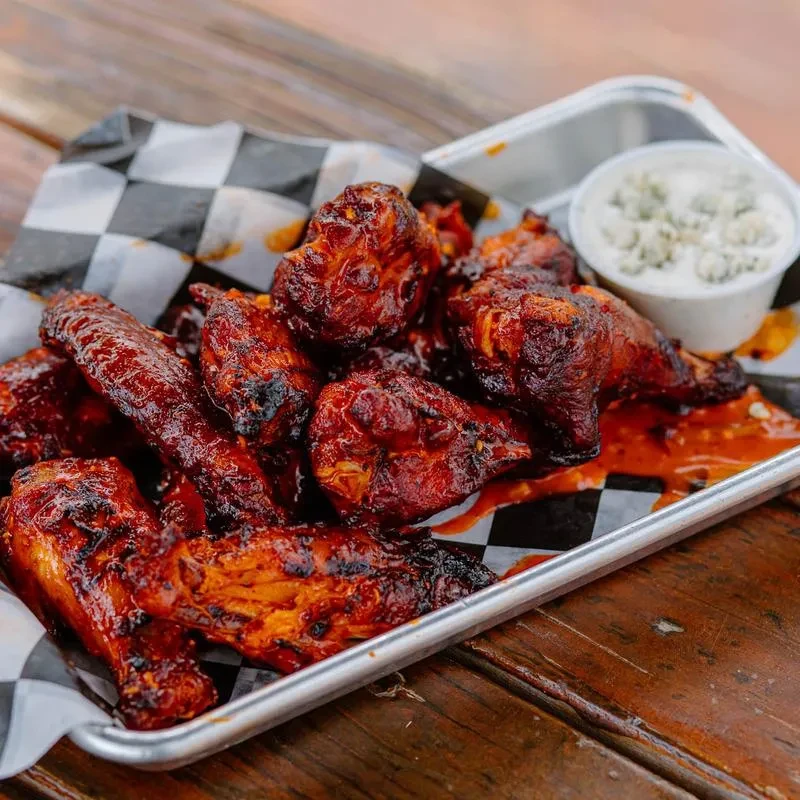 Glossy red chicken wings with creamy dipping sauce on a checkered tray.