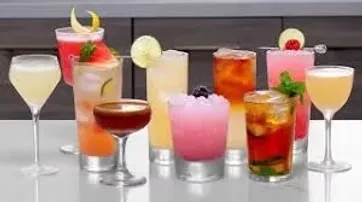 Ten diverse garnished cocktails in various glasses on a reflective surface.