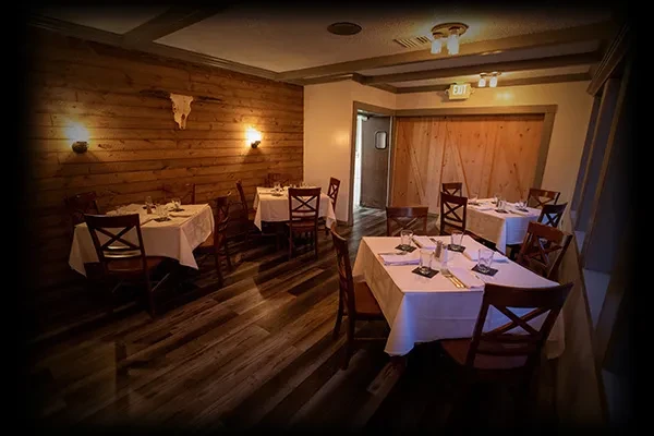 Rustic dining area with set tables, wooden walls, and steer skull.