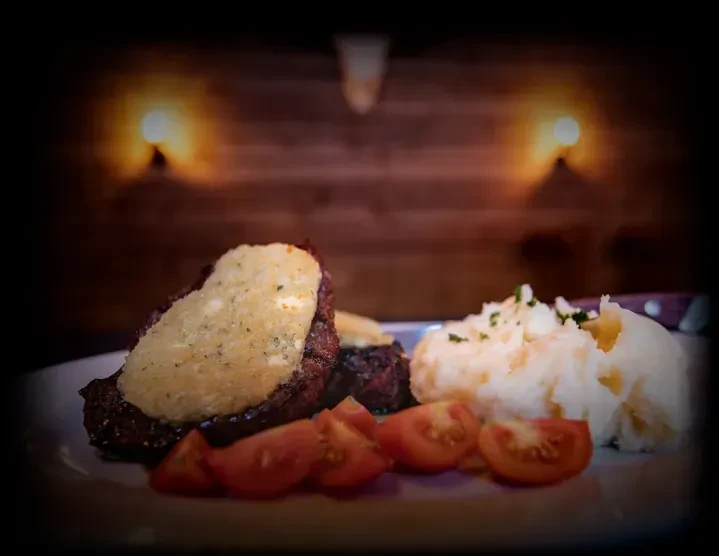 Seared meat with creamy sauce, mashed potatoes, and sliced tomatoes.