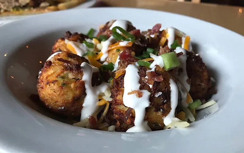 Golden-brown potato tots topped with cheese, bacon, sauce, and chives.
