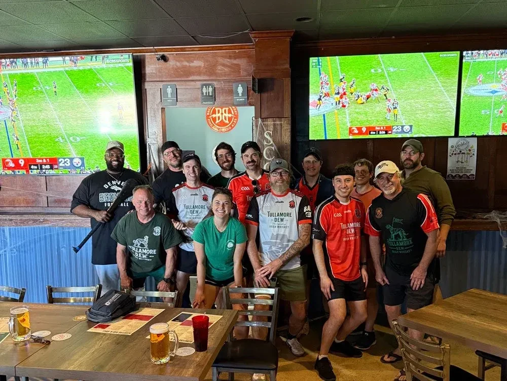 Fifteen smiling people pose in a sports bar showing football.