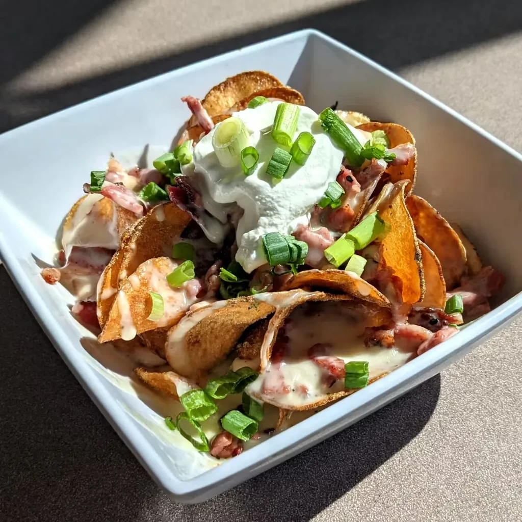 Loaded potato chips in a bowl with cheese, bacon, sour cream, chives.