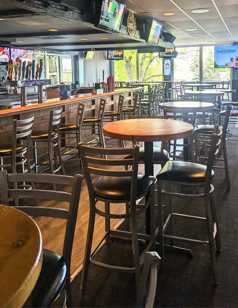 Empty bar interior with tables, beer taps, TVs, and large windows.