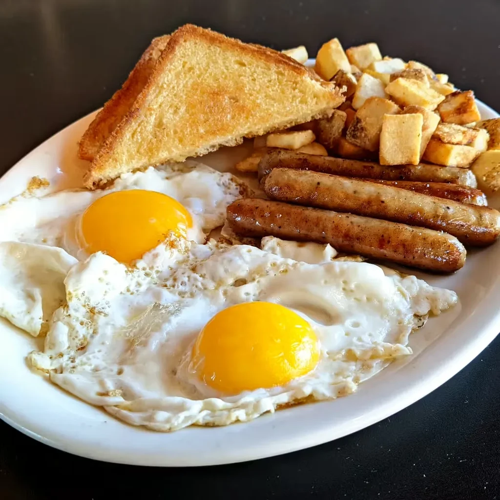 Breakfast plate with sunny-side-up eggs, sausages, home fries, and toast.