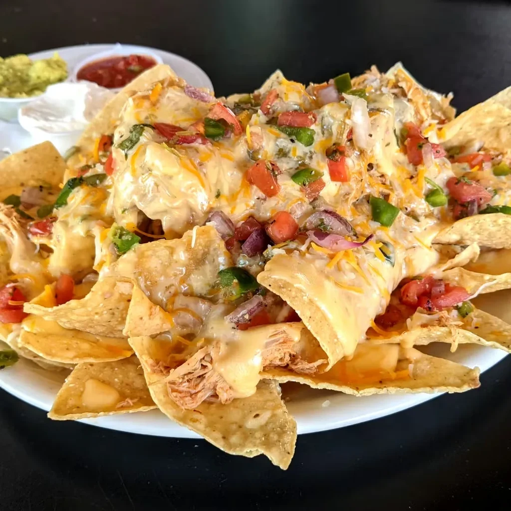 Close-up of nachos with melted cheese, chicken, vegetables, and dips.