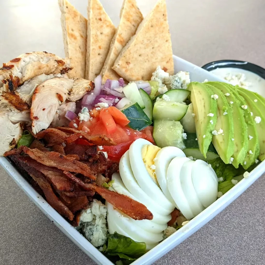 Colorful Cobb salad with chicken, bacon, egg, avocado, pita, and dressing.
