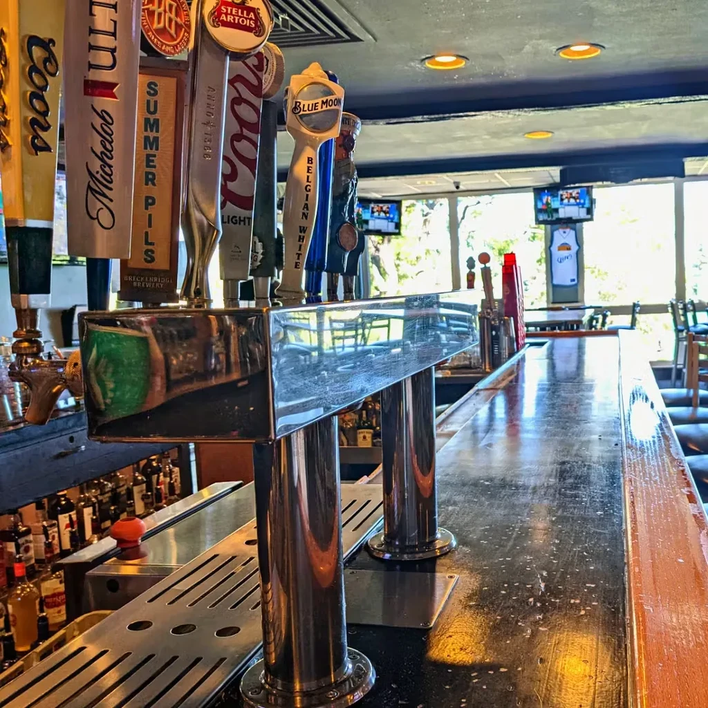 Polished chrome beer taps and liquor bottles on a dark bar counter.
