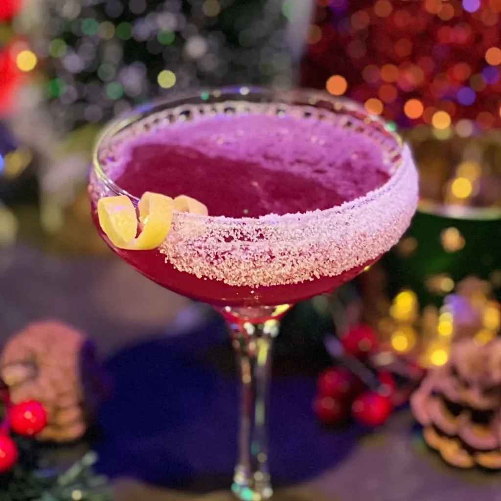 Frothy red holiday cocktail with snowy rim and lemon garnish.