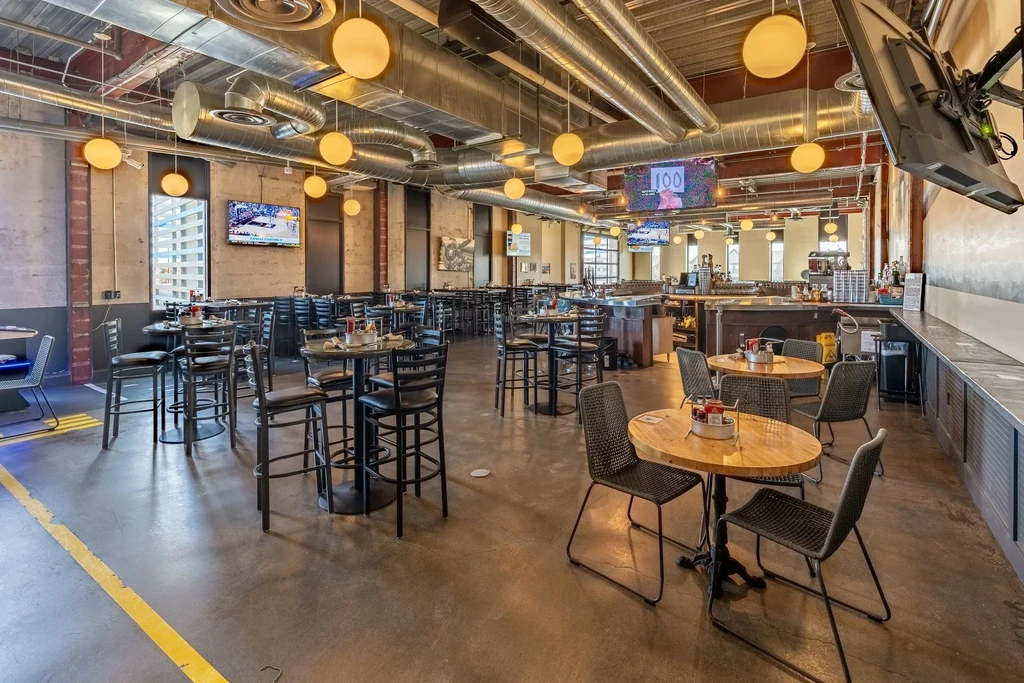 Modern industrial-chic restaurant interior with varied seating, bar, and sports screens.