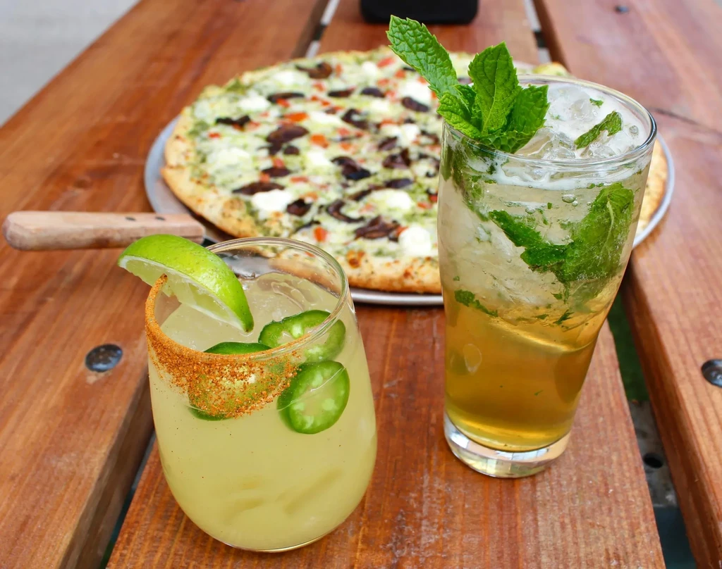 Two cocktails and a pizza on a rustic wooden table.