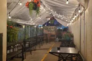 Restaurant patio at night with string lights, plants, and black tables.